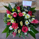Corona fúnebre hecha con flores naturales blancas y rosadas con follajes verdes.