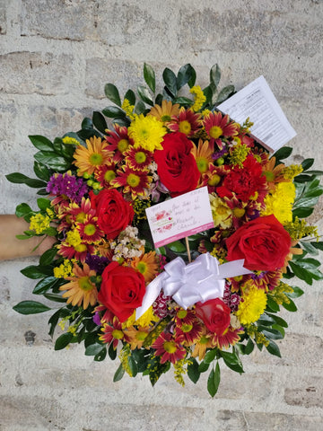 Corona fúnebre pequeña con flores naturales amarillas y rojas con follajes verdes.