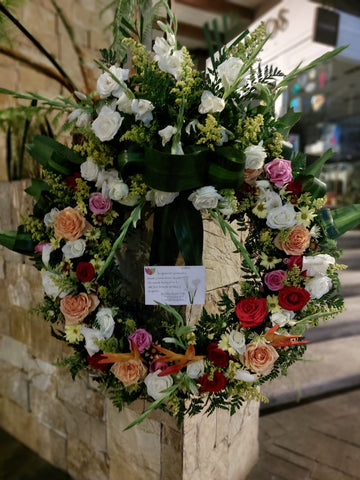 Elegante corona fúnebre con rosas amarillas y rojas.