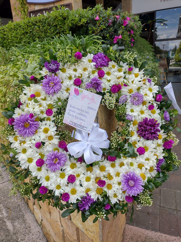 Corona con flores lilas y blancas con follajes verdes.