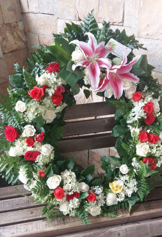 Corona fúnebre con lirios, rosas y hortensias con follajes verdes.