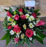 Corona fúnebre pequeña hecha con flores naturales blancas y rosadas con follajes verdes.