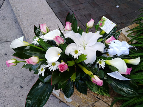 Palmatoria hecha con flor de lirio, rosas, cartuchos y follajes verdes.