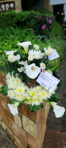 Corona de flores blancas como rosas, cartuchos y follajes verdes.