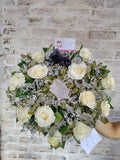 Elegante corona fúnebre hecha con rosas blancas y eucaliptos.