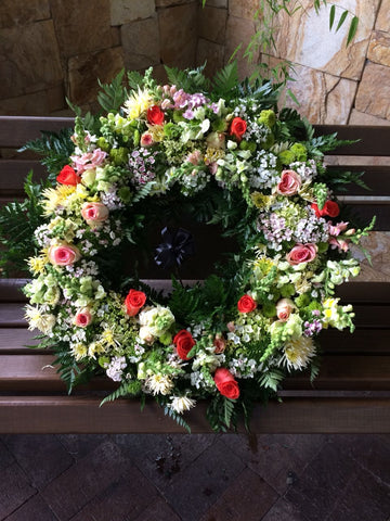 Corona fúnebre con flores rojas, blancas, lilas.