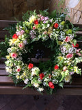 Corona fúnebre con hojas verdes, flores rojas, blancas, lilas.
