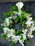 Corona fúnebre con flores artificiales, orquídeas de color blanco, cartuchos y follajes verdes.