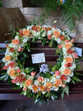 Corona fúnebre con hojas y flores naturales: anaranjadas, blancas, rojas.