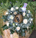 Corona fúnebre hecha con rosas blancas y eucaliptos.