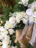 Corona blanca para difunto con flores artificiales blancas y hojas verdes.