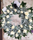 Elegante corona fúnebre con rosas blancas y eucaliptos.