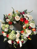 Corona fúnebre hecha con flores naturales: anaranjadas, blancas, verdes