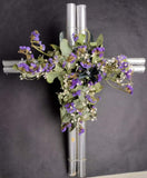Linda cruz plateada con flores artificiales lilas y verdes.