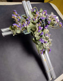 Preciosa cruz plateada con flores artificiales lilas y verdes.