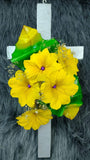 Linda cruz de madera con flores artificiales amarillas y hojas verdes.