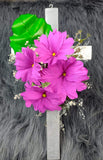 Linda cruz de madera con flores artificiales lilas y hojas verdes.