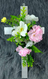 Linda cruz de madera con flores artificiales rosadas y blancas, con hojas verdes.