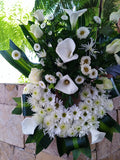 Corona de flores blancas hechas con rosas, cartuchos y follajes verdes.