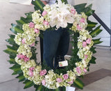 Corona fúnebre con hojas verdes y flores blancas y rosadas
